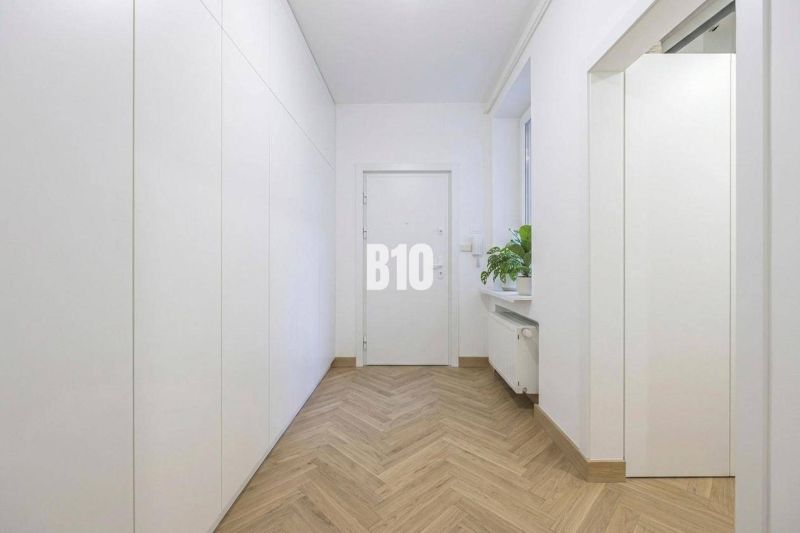 A cozy hallway with white walls, a wooden decor floor, and a plant in a 3-room apartment.