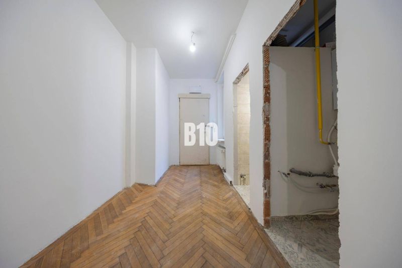 A hallway in a 3-room apartment with a wooden decor floor and piping in the wall.