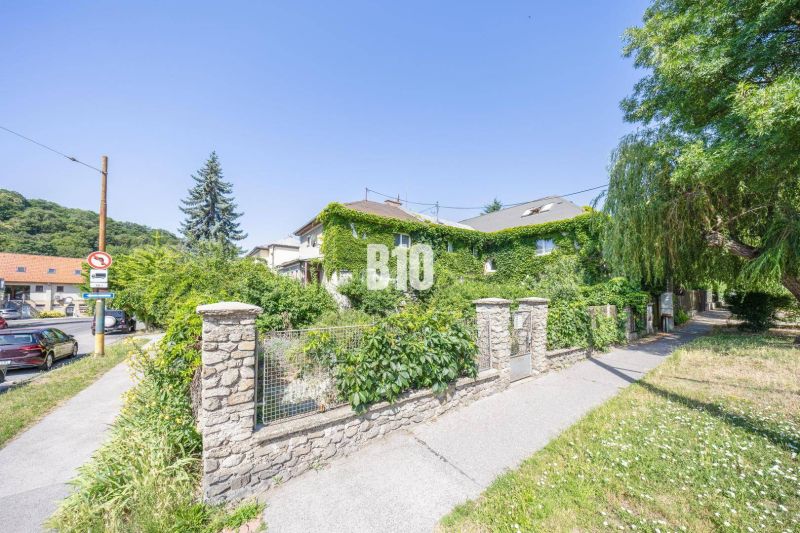 A family house in Bratislava - Old Town covered with greenery, surrounded by a stone fence and trees.
