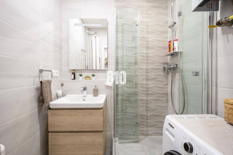 Bathroom in a 2-room apartment with a washing machine, sink, and shower.