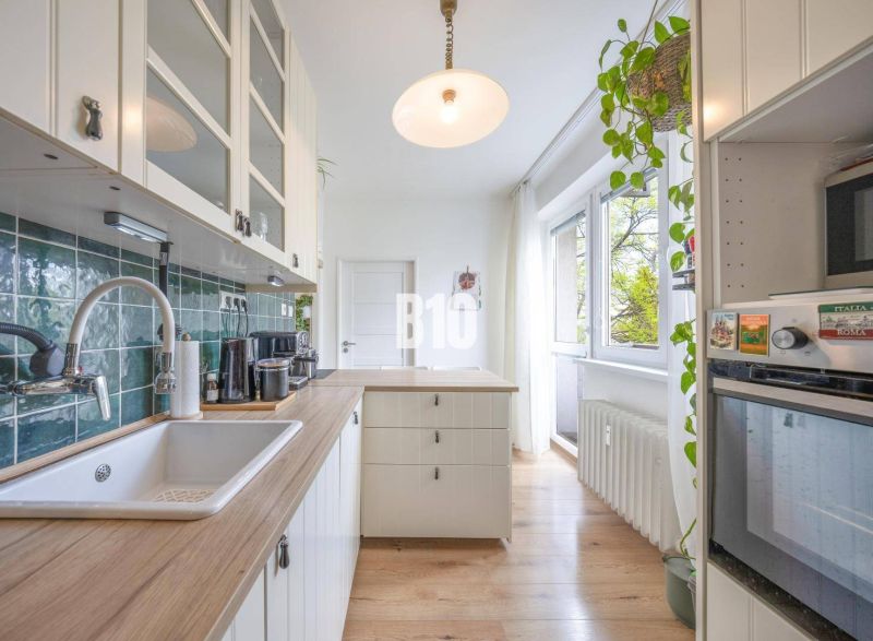 A kitchen in a 2-room apartment with a wooden decor floor and white cabinets.