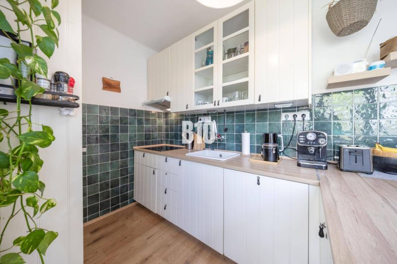 A kitchen in a 2-room apartment with a wooden decor floor and green tiles.