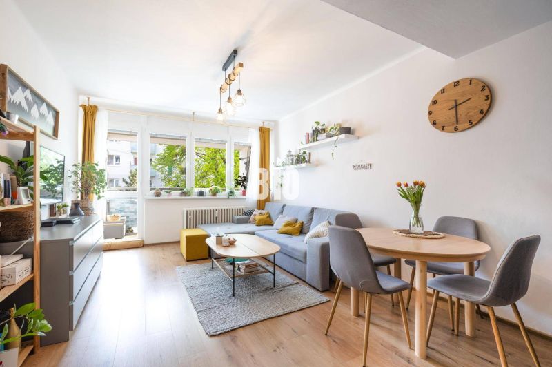 Interior of a 2-room apartment with wood-patterned flooring, a sofa, and a dining area.