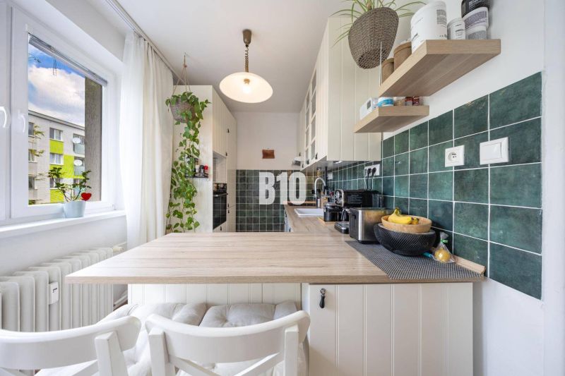 A kitchen in a 2-room apartment with a kitchen unit, wooden decor, and green tiles.