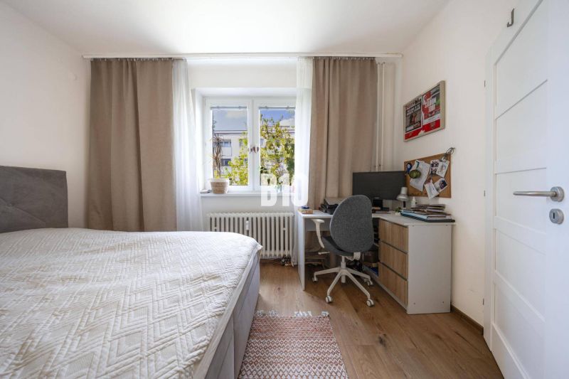 A bedroom in a two-room apartment with a desk and a wooden floor.