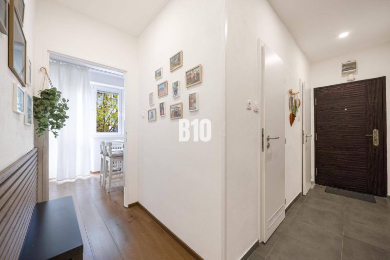 A hallway in a 2-room apartment with a wood-patterned floor and white walls.