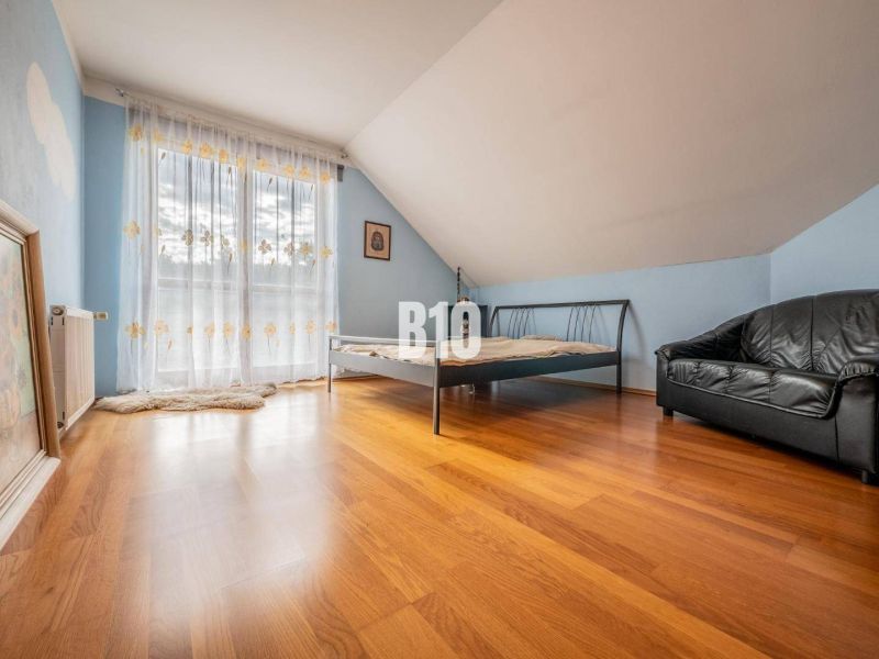 Bedroom in a family house with a bed, leather sofa, and wooden floor.