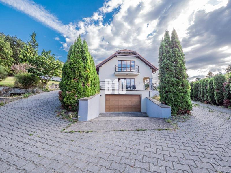 A family house in Marianka with shrubbery lining, a garage, and a partly cloudy sky.