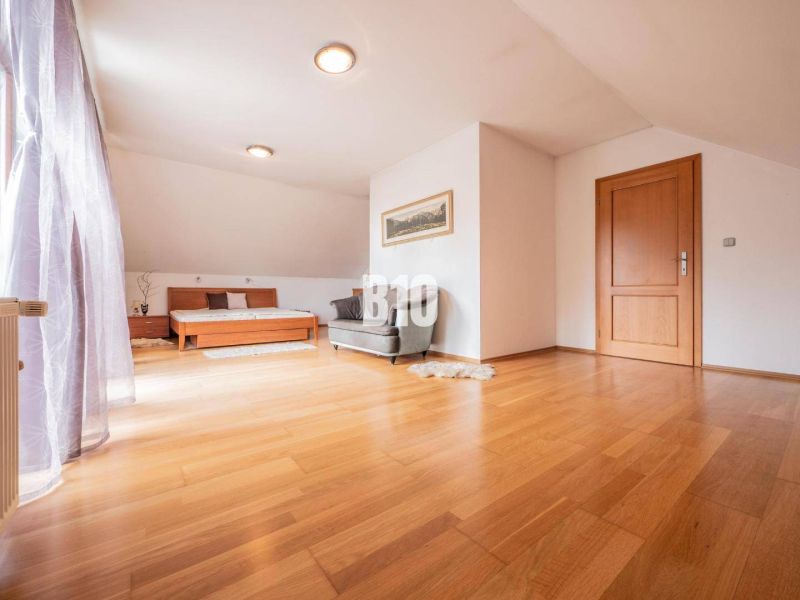 Spacious bright room, wooden floor, bed and chair, family house.
