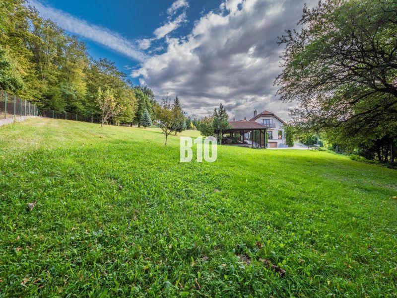 A family house in Marianka with a garden and a forest backdrop under a blue sky.