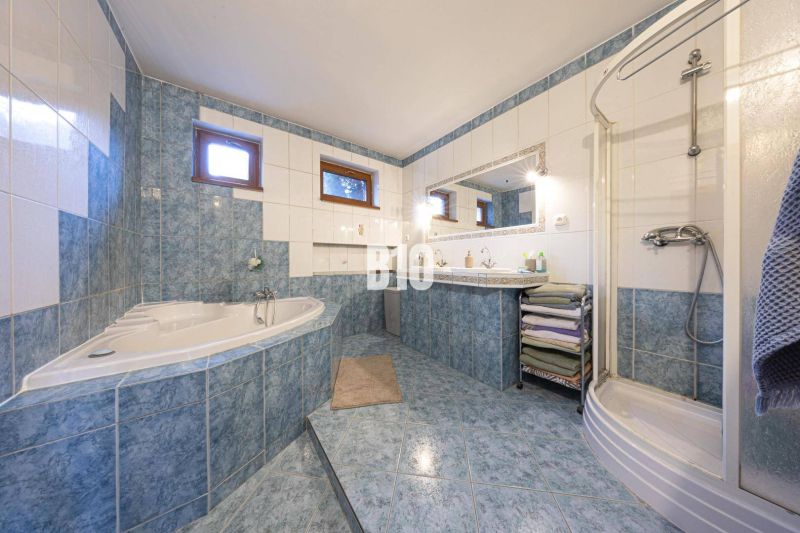 A bathroom in a family house with a bathtub, a shower corner, and blue ceramic tiles.