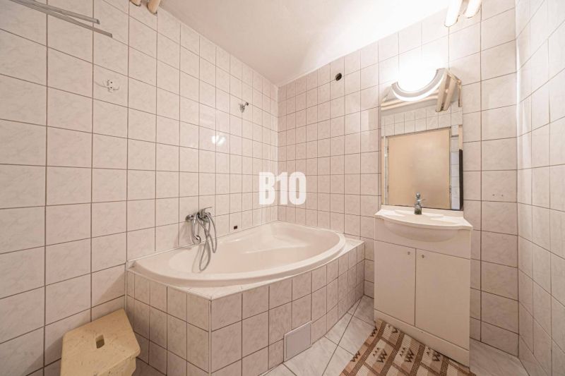 A bathroom with a bathtub and a sink in a family house, tiled with light tiles.