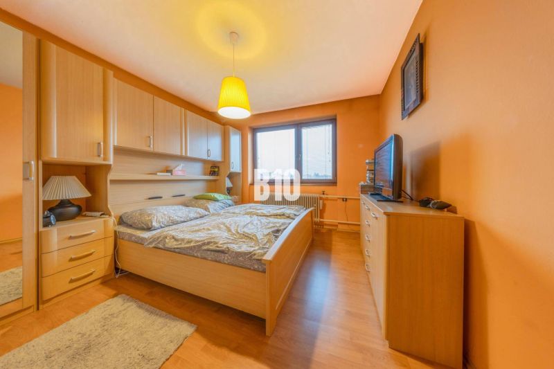 A bedroom in a family house with orange walls and a wood-patterned floor.