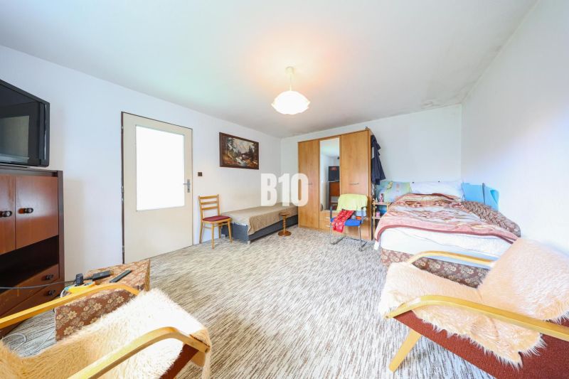 A room with a bed, cabinets, and an armchair in a family house. A carpet covers the floor.