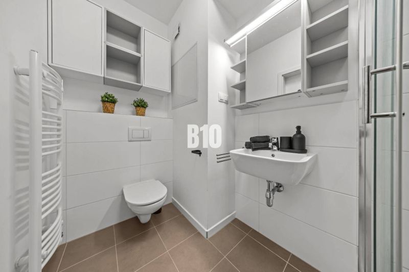 A bathroom in a studio apartment with white sanitary ware and storage spaces.
