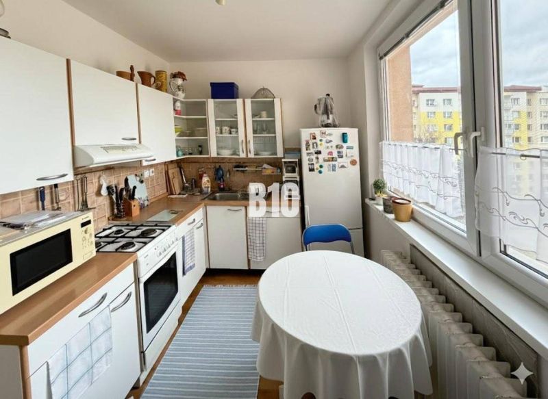 A kitchen in a 3-room apartment with a table, a refrigerator, and a kitchen unit with a sink.