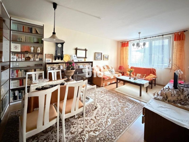 Living room with a dining table and shelves in a three-room apartment with a wooden decor floor.