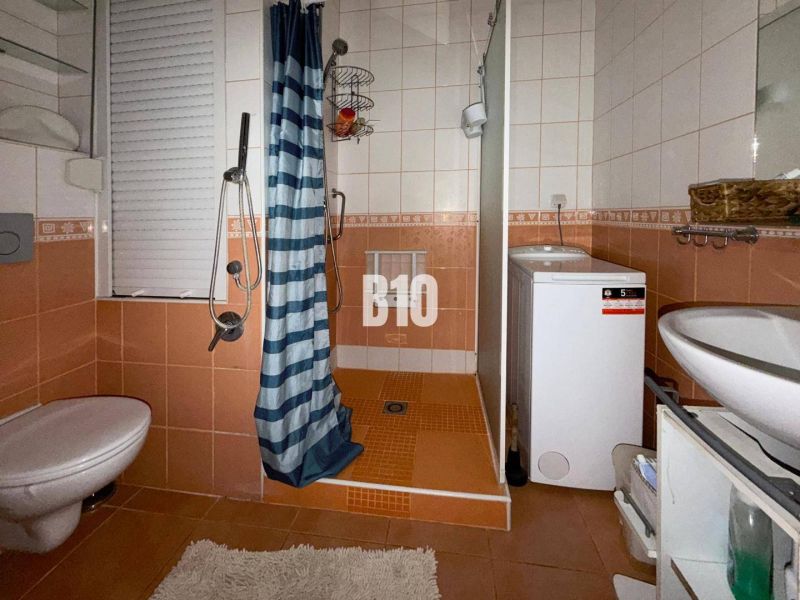A bathroom in a 3-room apartment with orange tiles, a shower, a washing machine, and a toilet.