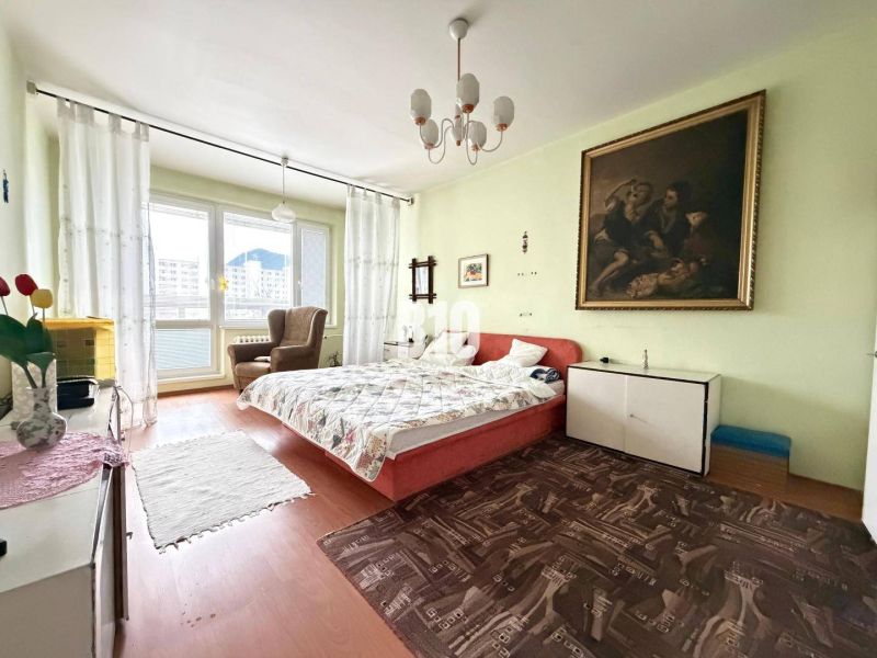 A room with a double bed, a painting on the wall, and a floor with a wooden decor.