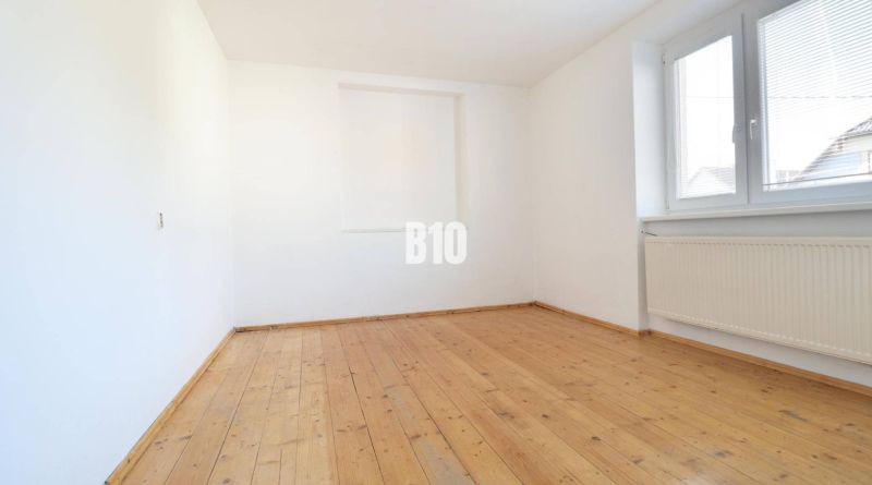 A bright room with a wood-patterned floor and a large window in a family house.