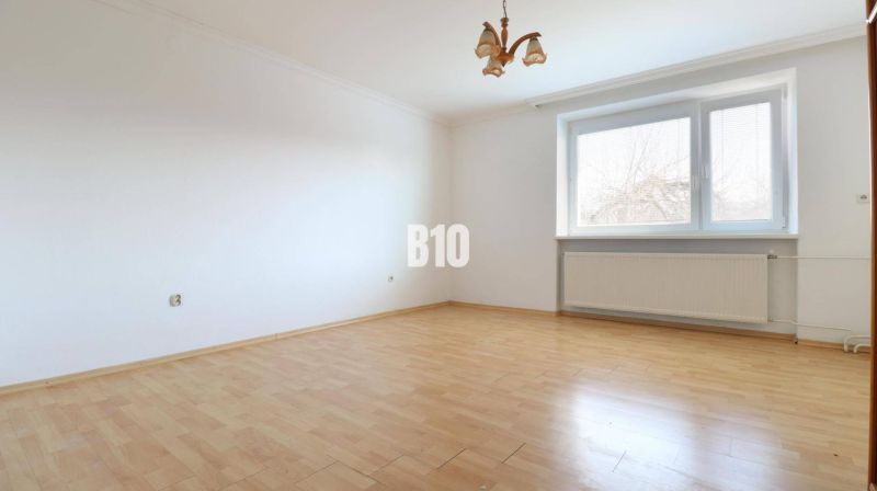 An empty room in a family house with a wood-patterned floor and a large window.