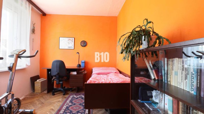 A room in a 3-room apartment with furnishings: bed, table, shelf, and exercise bike.