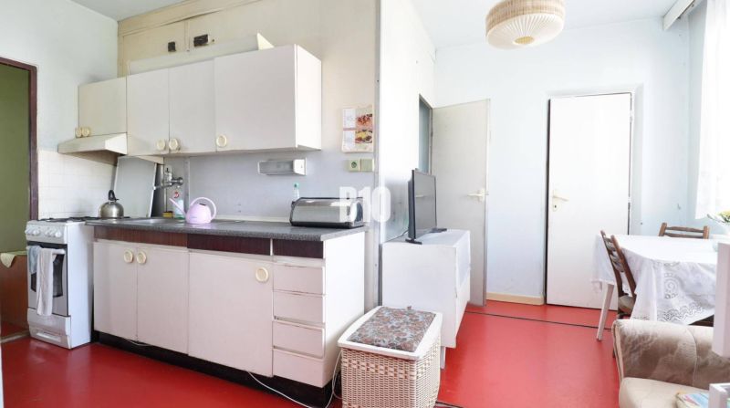 A kitchen in a 3-room apartment with white furniture and a red floor.