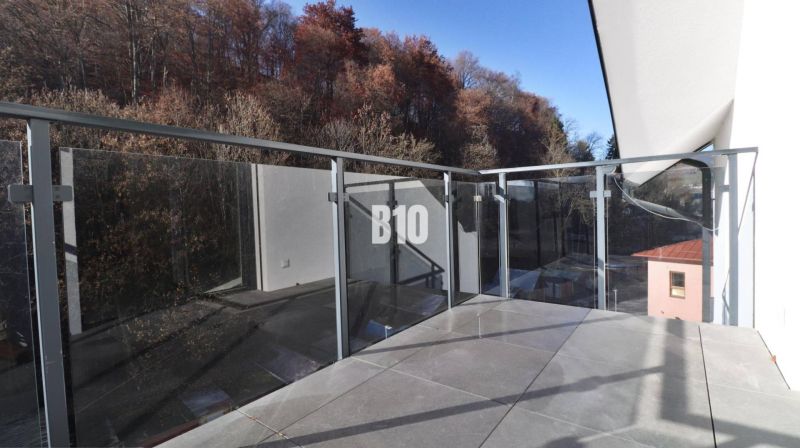 A balcony of a 2-room apartment in Dolný Kubín with glass railing and surrounded by trees.