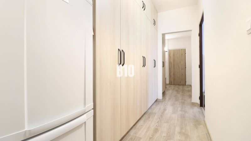 A hallway in a 3-room apartment with a wooden decor floor and light-colored cabinets.