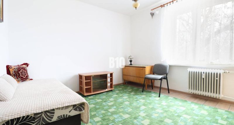Interior of a 3-room apartment with carpeted flooring, an armchair, and a lamp by the window.