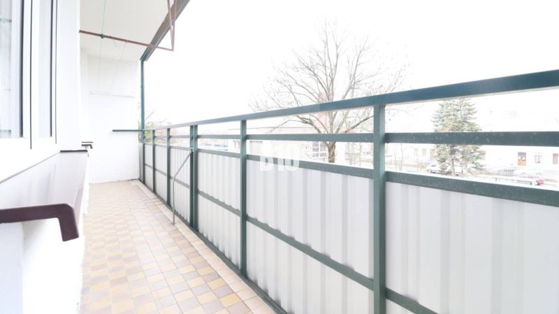 Balcony of a 3-room apartment with a view of trees and paving.