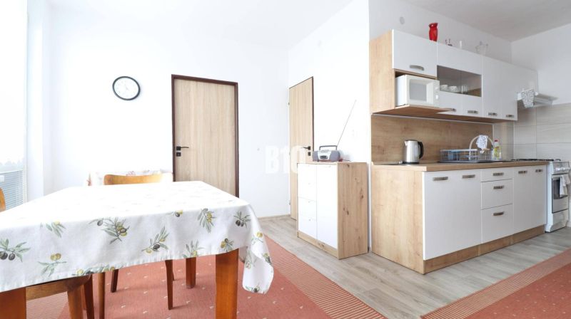 A kitchen in a 3-room apartment with a wood-patterned floor, a dining table, and cabinets.