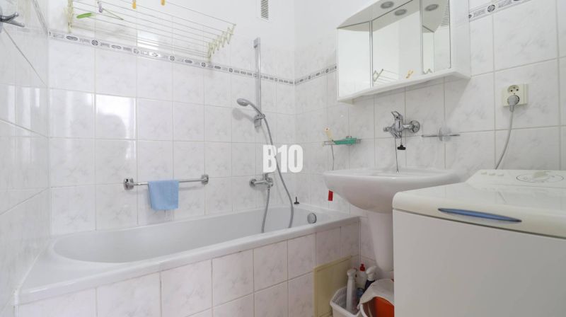 A bathroom in a 3-room apartment with a bathtub, sink, mirror, and washing machine.