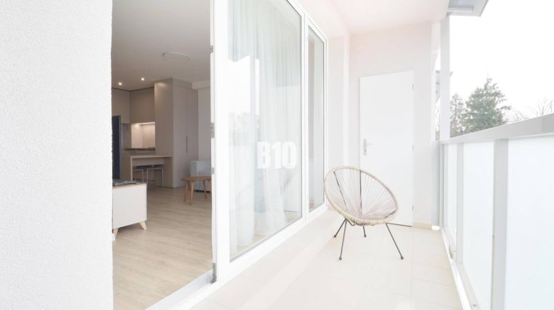 A balcony with a view into a studio apartment, wooden decor flooring, cozy seating.