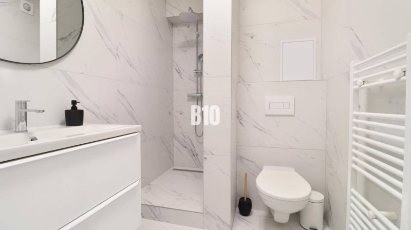 A bathroom with white tiles and a shower in a studio apartment.