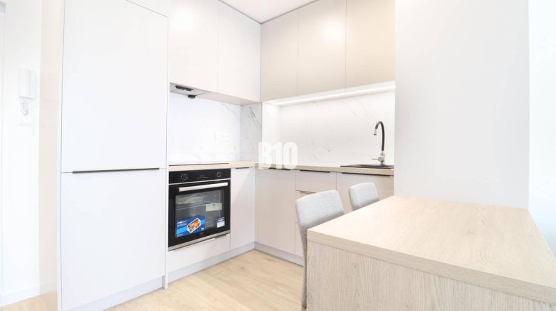 A kitchen in a studio apartment with wooden floor decor and modern appliances.