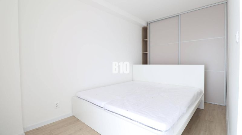 Bedroom in a studio apartment with a bed, built-in wardrobe, and wooden decor flooring.
