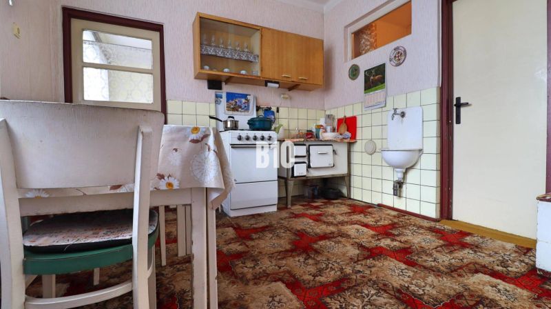 A kitchen in a family house with a tiled stove and a reddish-brown carpet.