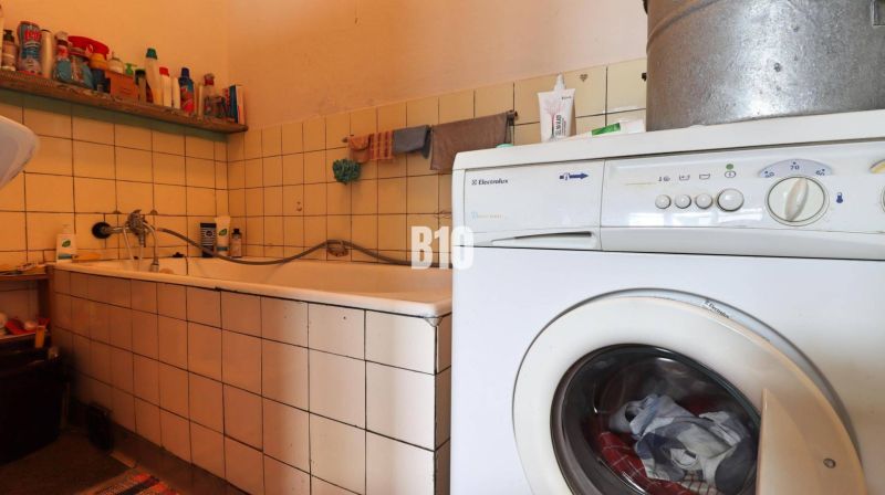 A bathroom in a family house with a bathtub, a washing machine, and cleaning products on a shelf.