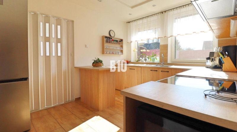 A kitchen in a family house with wooden decor, light furniture, and a window letting in daylight.