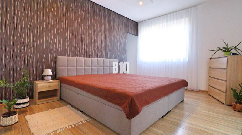 Bedroom with a bed, wallpapered wall, wooden floor decor, and furniture in a family house.
