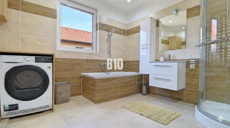 Bathroom in a family house with a bathtub, shower, and washing machine, floor with a wooden decor.