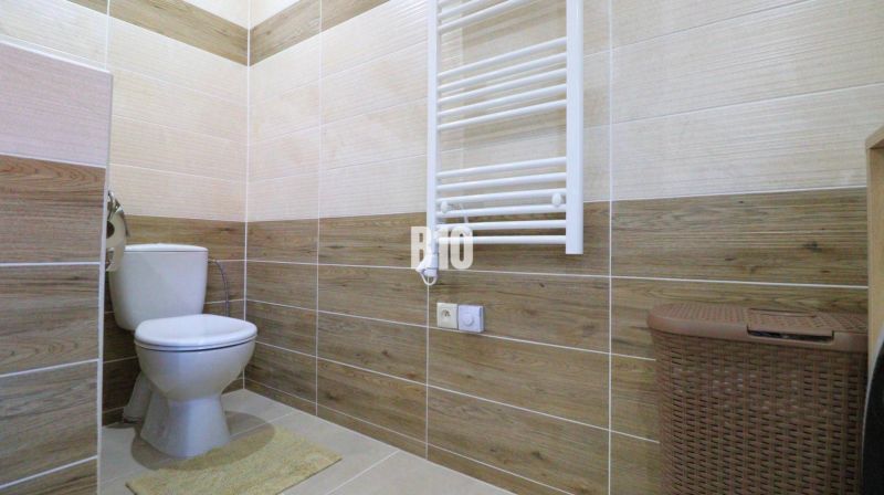 Bathroom with toilet, wood-patterned tiles, radiator, basket, wood-patterned floor.