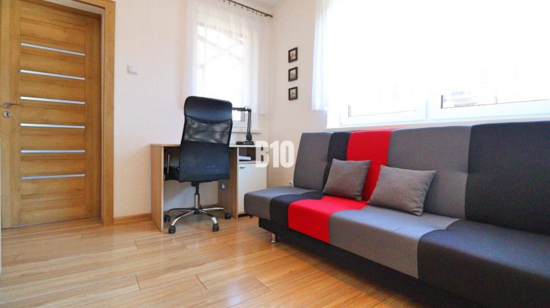 A room in a family house with a desk, chair, and colorful sofa, wooden decor flooring.