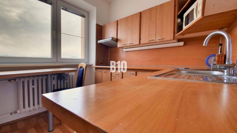 A kitchen in a studio apartment with a wood-patterned floor and a view from the window.