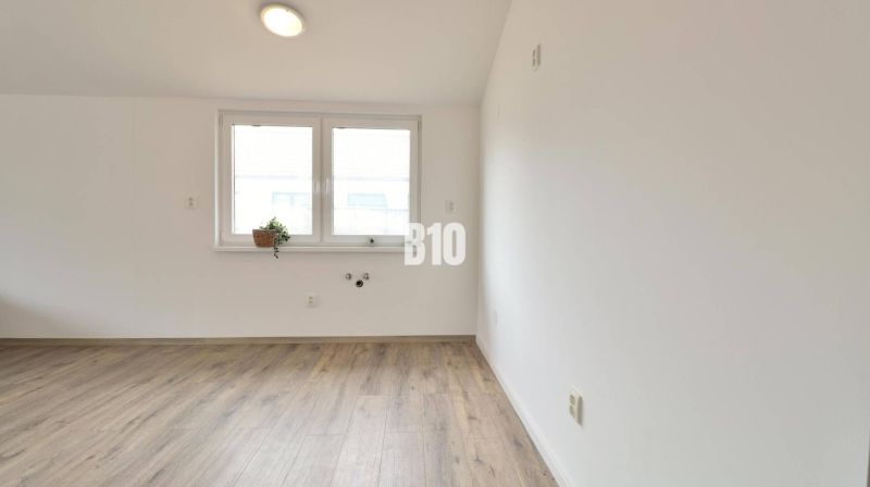 An empty room in a family house with a wood-patterned floor and a window.