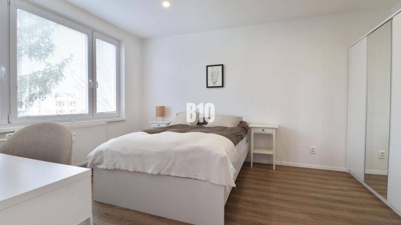 A bright bedroom with wood-decor flooring in a three-room apartment with a built-in wardrobe.