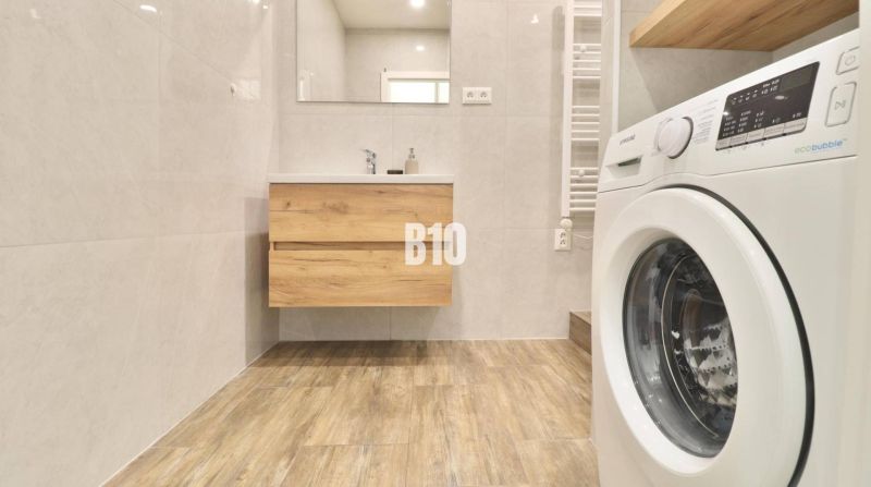 A bathroom in a 3-room apartment with a washing machine and a wooden decor floor.