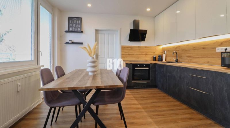 A kitchen in a 3-room apartment with a wooden decor, a table, and colorful chairs.