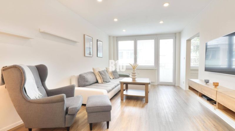 Living room with a sofa, armchair, and wooden decor flooring in a 3-room apartment.